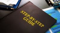 Schwarze Mappe mit Aufschrift "step by Step Guide" auf Tisch liegend