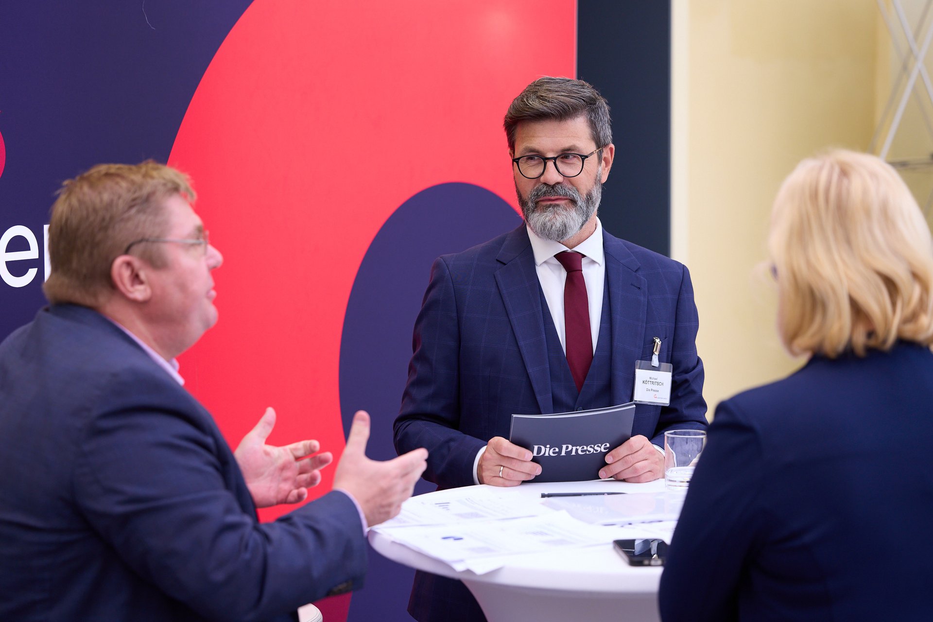 Gespräch an einem Stehtisch zwischen zwei Herren in Anzug und einer blonden Dame