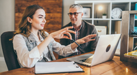 Young woman explains something to an older man in front of a computer